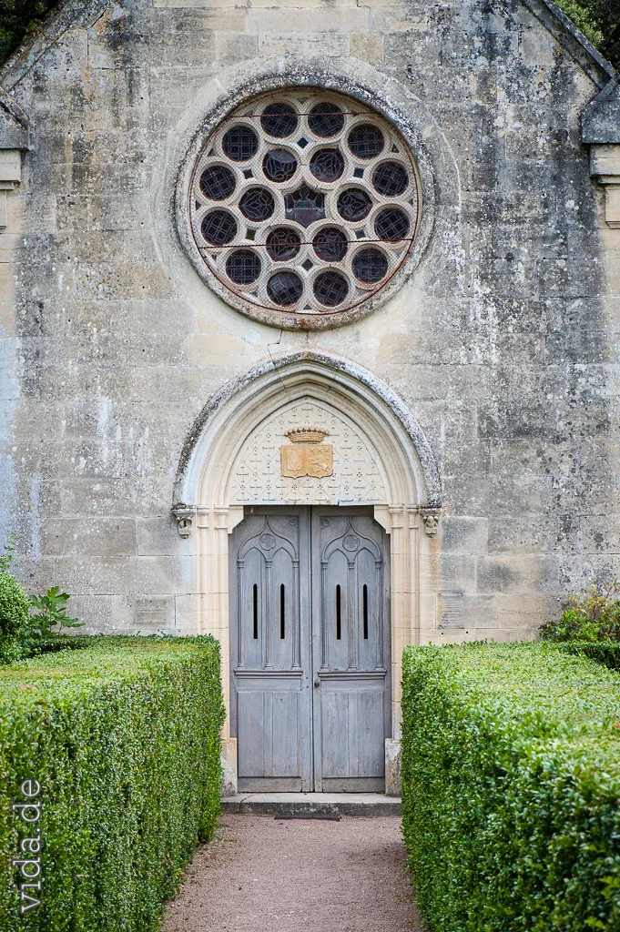 Kapellenportal mit Rosettenfenster, gesäumt von Hecken