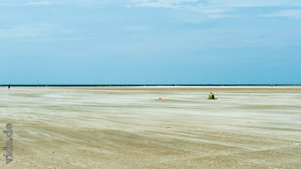 Flacher Strand bis zum Horizont, ein Fahrzeug winzig in der Ferne