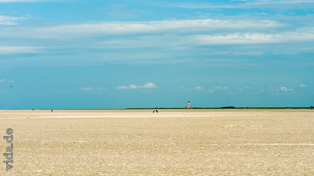 Heller Sandstrand mit Spaziergängern klein am Horizont, darüber Schleierwolken