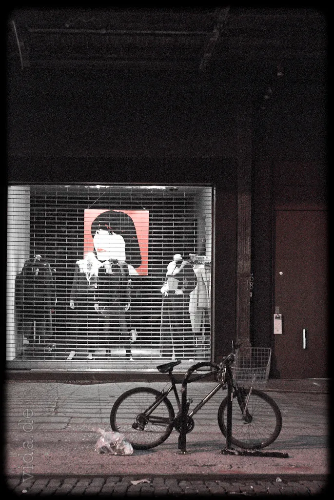 Fahrrad vor einem Schaufenster mit Plakat, schwarzweiß mit einem roten Akzent